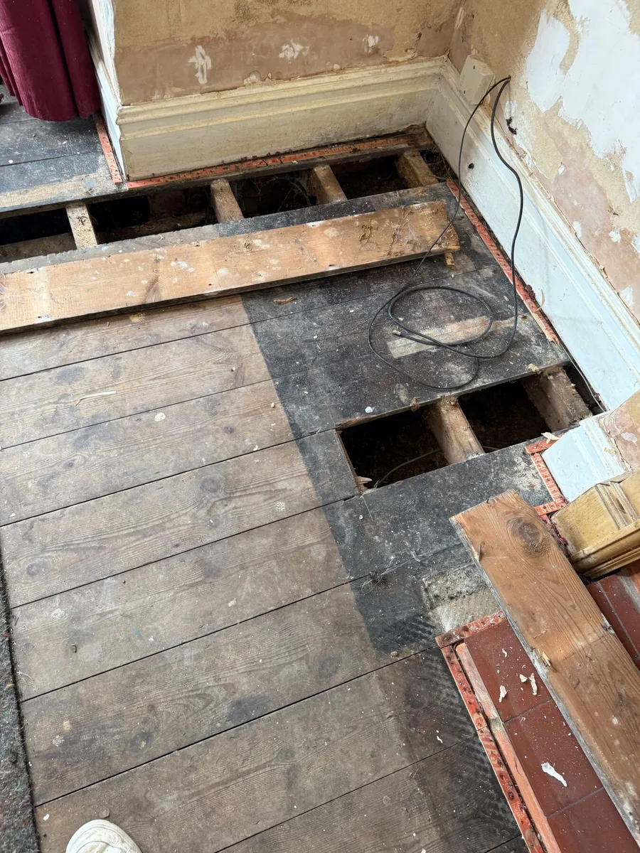 Exposed floor joists and damp damage beneath floorboards